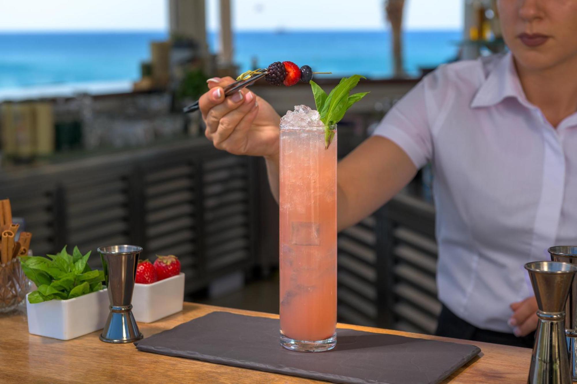 ホテル ロドス パラディウム レジャー ＆ ウェルネス Kallithéa エクステリア 写真 A bartender garnishes a cocktail with a fruit skewer.